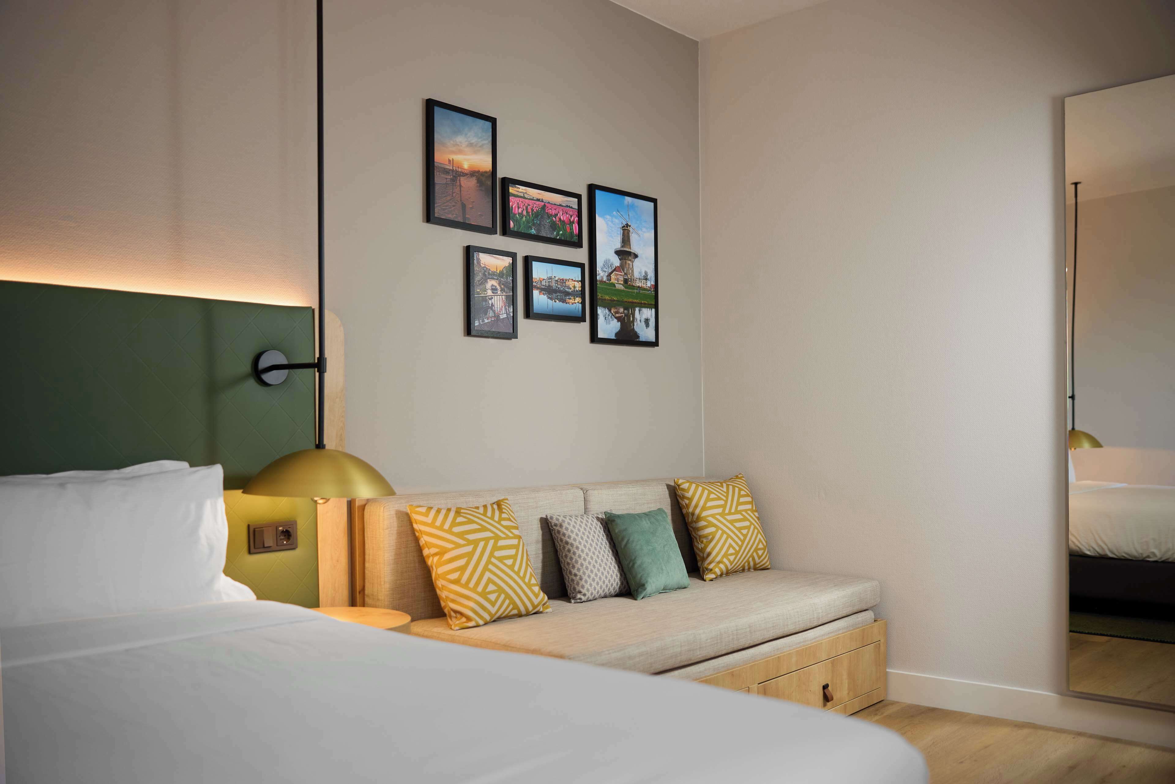 Una habitación de hotel con cama, sofá, mesita de noche y una pared decorada con cuadros.