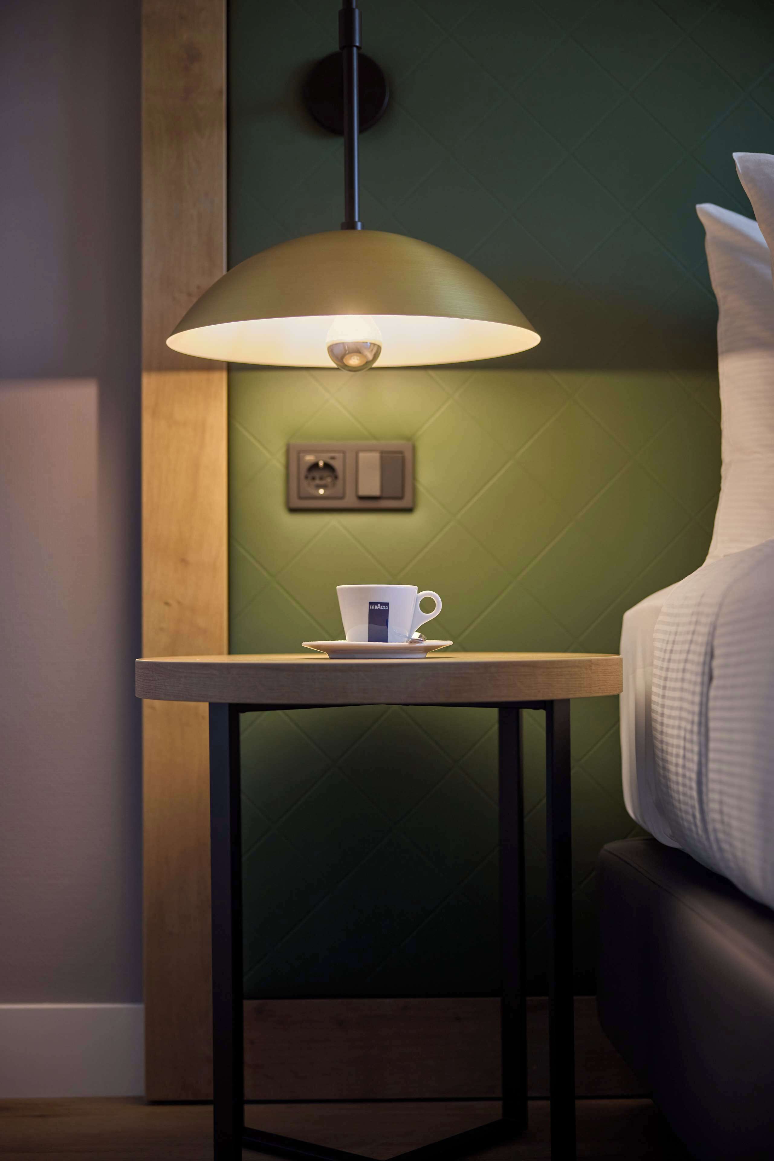 A room with a table, a lamp, a cup, and a bed.