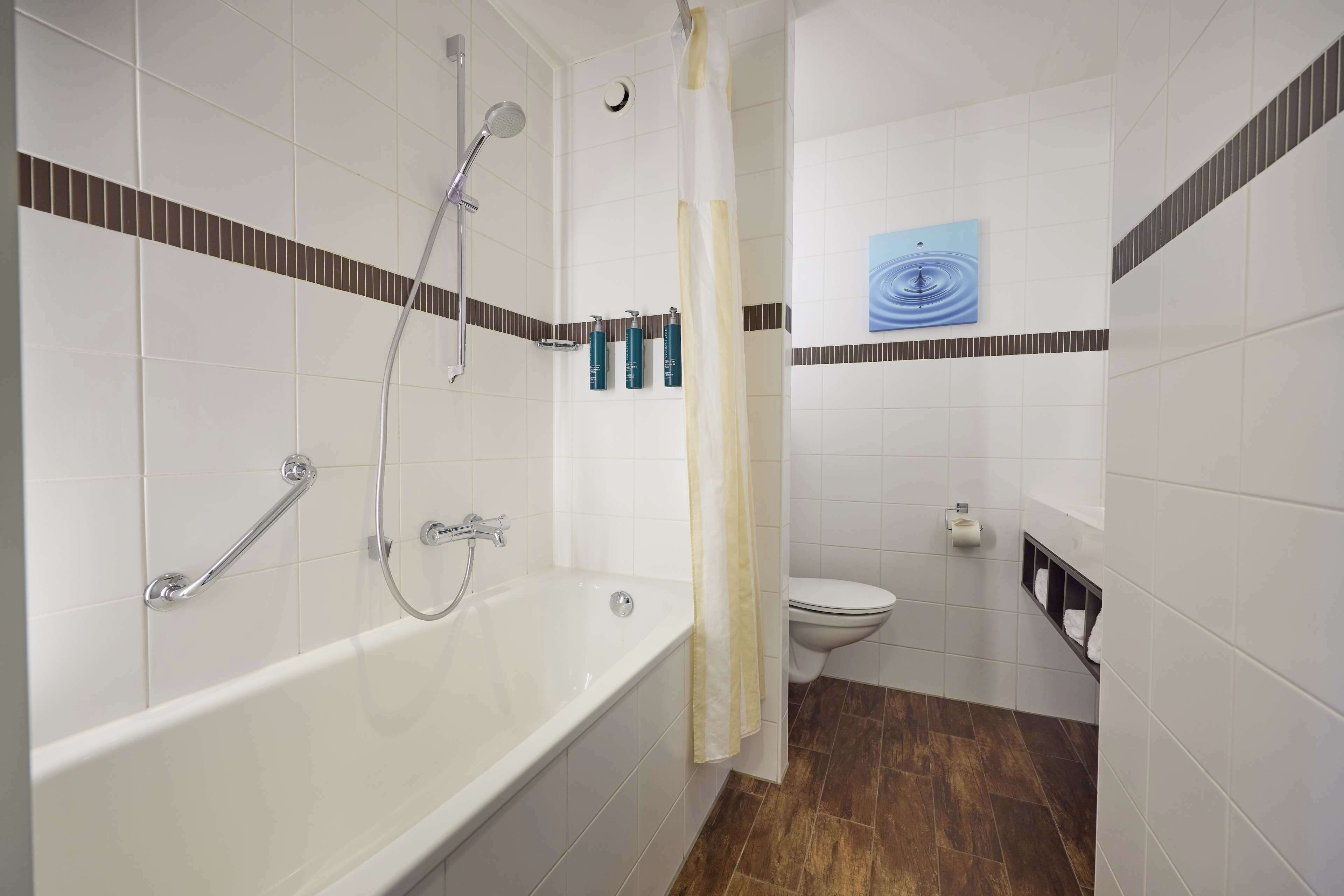 A bathroom with a bathtub, shower, toilet, and a towel rack.