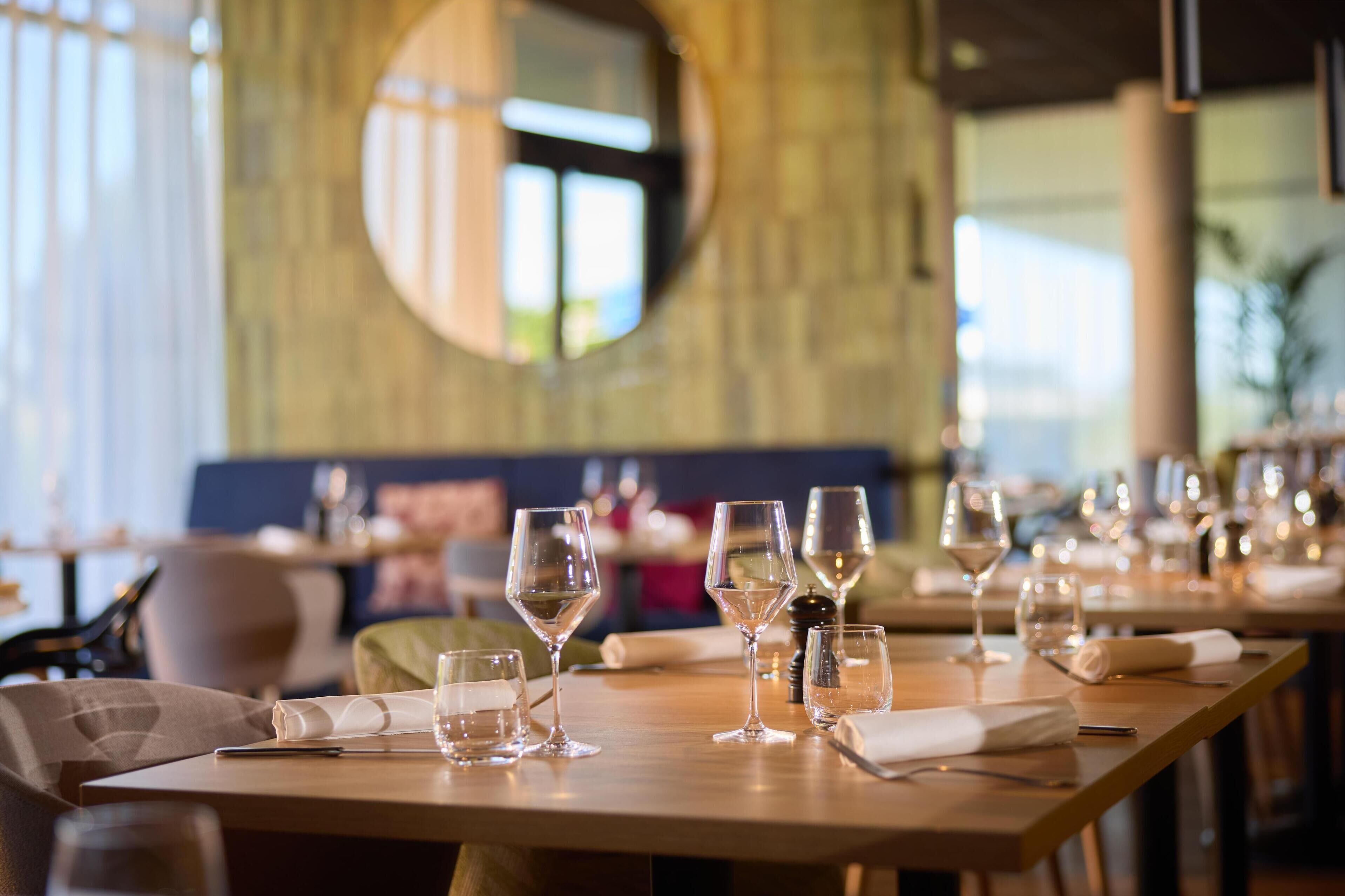 A restaurant interior with round tables, clear glasses, and neatly folded napkins.