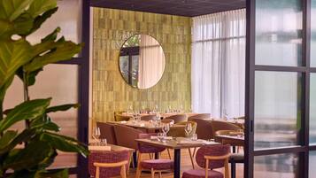Un restaurante con una decoración moderna, que incluye una pared verde con espejo, mesas de madera y sillas tapizadas en color púrpura.