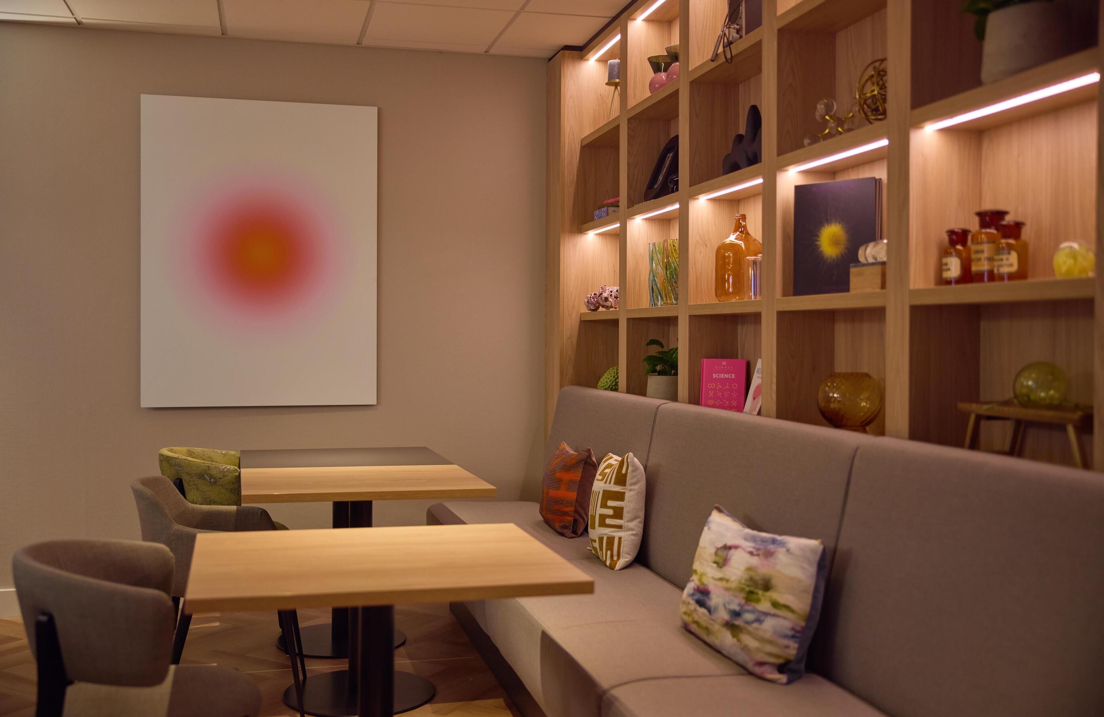 A modern lounge area with a sofa, two wooden tables, and a bookshelf with various decorative items.