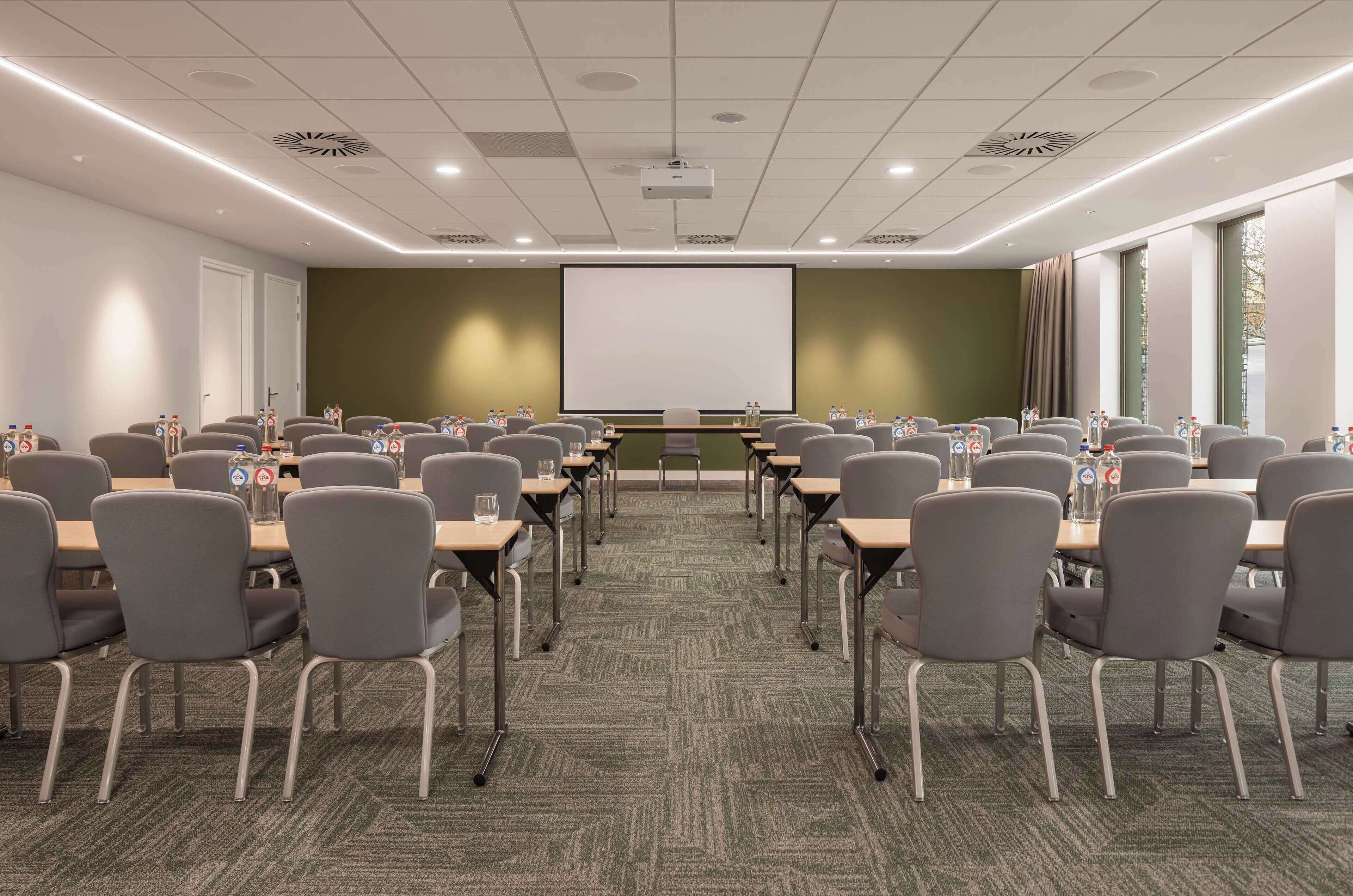 A conference room with rows of chairs, a projector screen, and a carpeted floor.