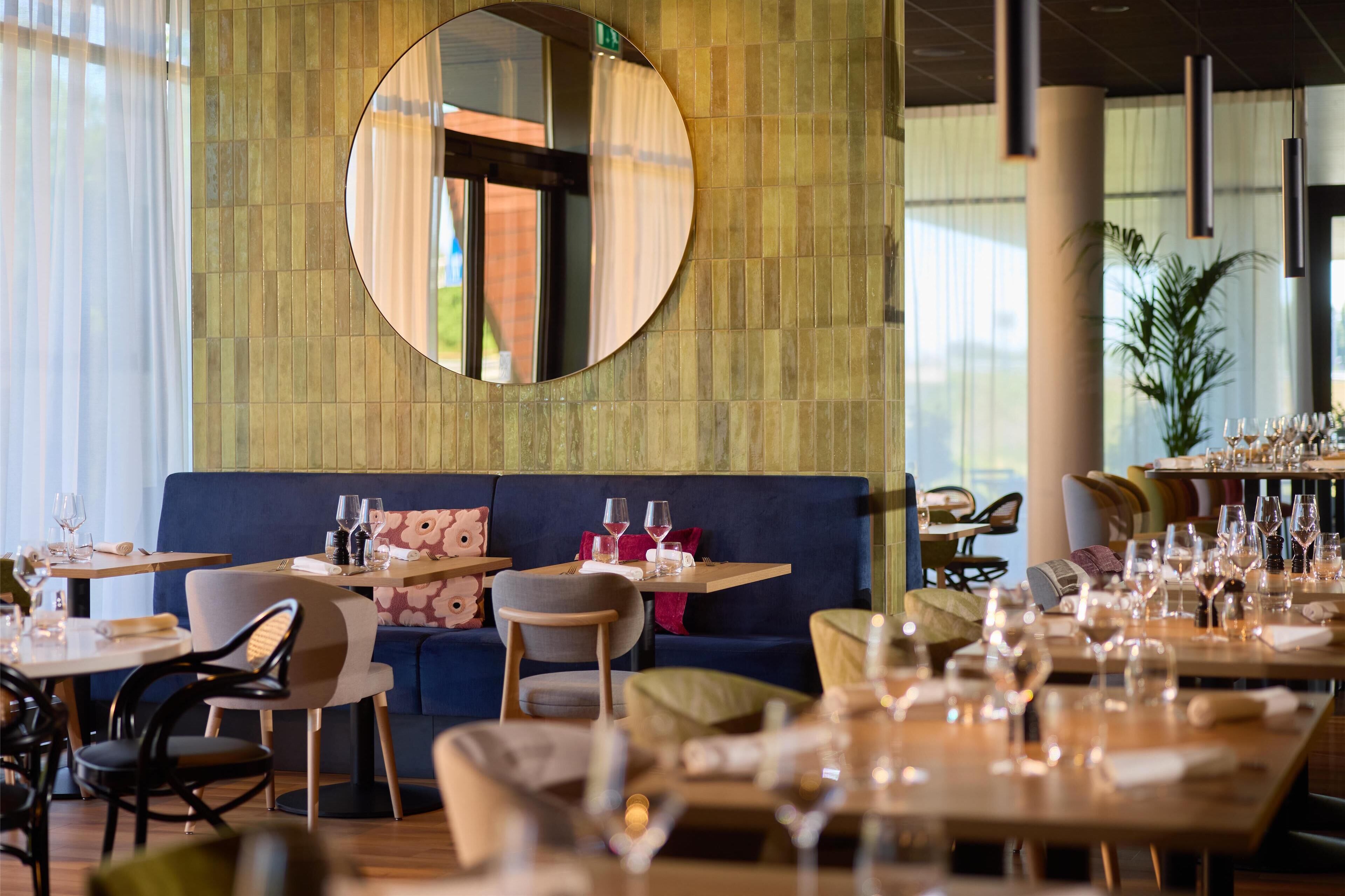 A restaurant interior with round tables, blue seating, and a large mirror on the wall.