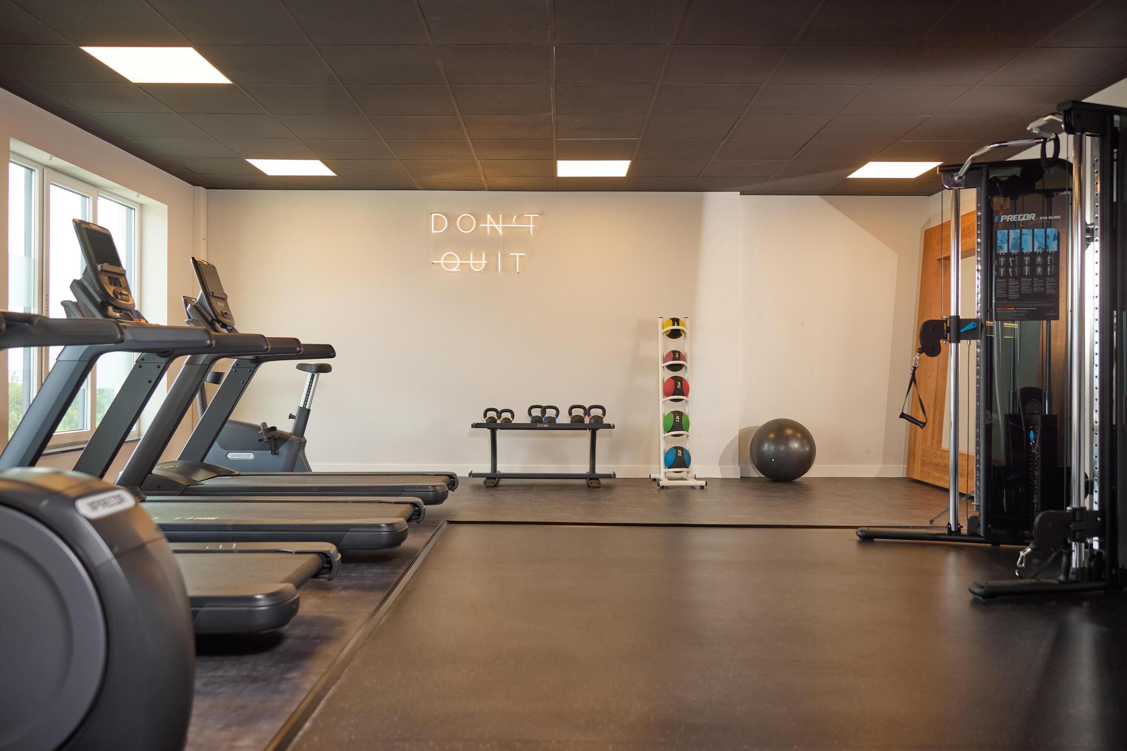 A gym with treadmills, a wall with motivational text, a bench, kettlebells, and a medicine ball.