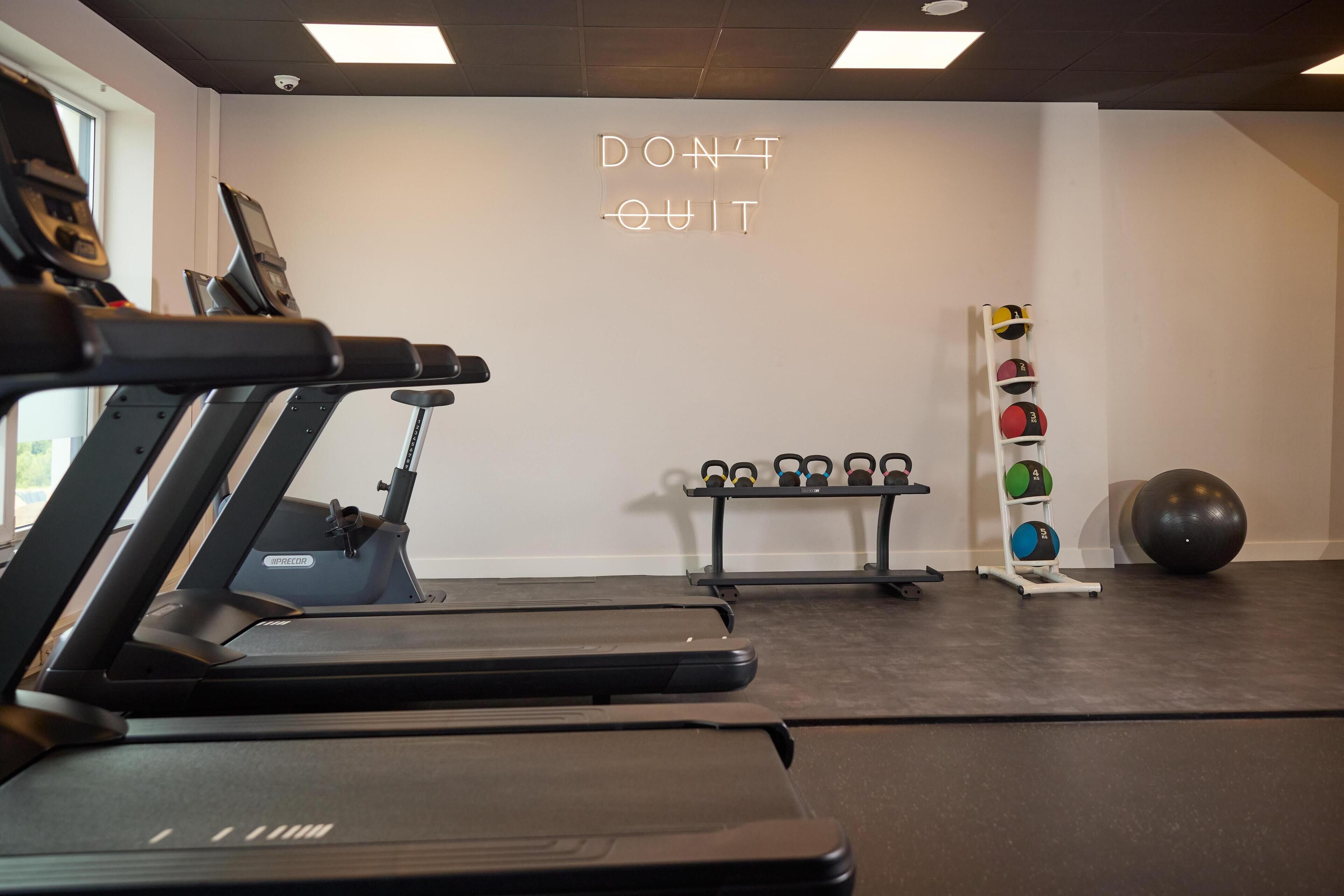 Ein Fitnessraum mit Laufbändern, einem an der Wand befestigten Motivationsschild, einem Kettlebell-Ständer und einem großen Trainingsball.