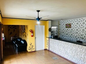 A room with a black leather sofa, a white door, a ceiling fan, and a patterned wall. - Nevada Ubatuba Hotel (Ubatuba)