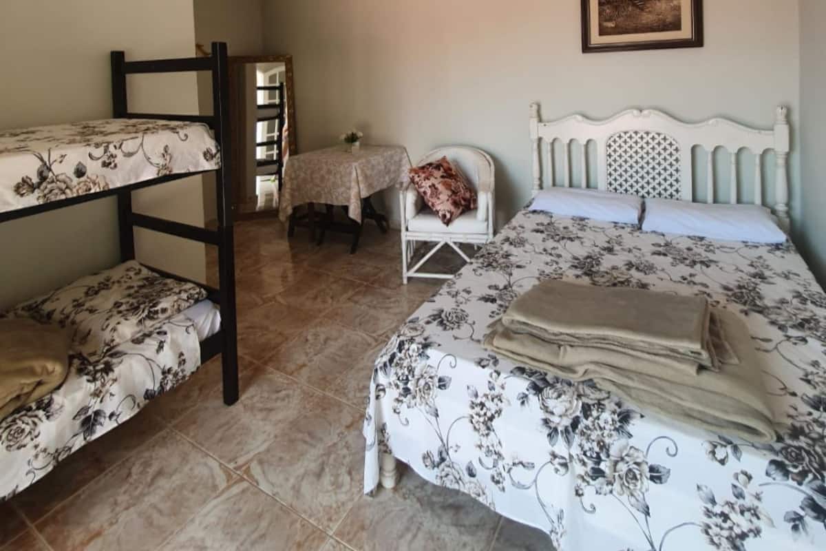 Une chambre avec des lits superposés, un lit simple, une table avec une chaise, un ventilateur de plafond et un tableau encadré au mur.