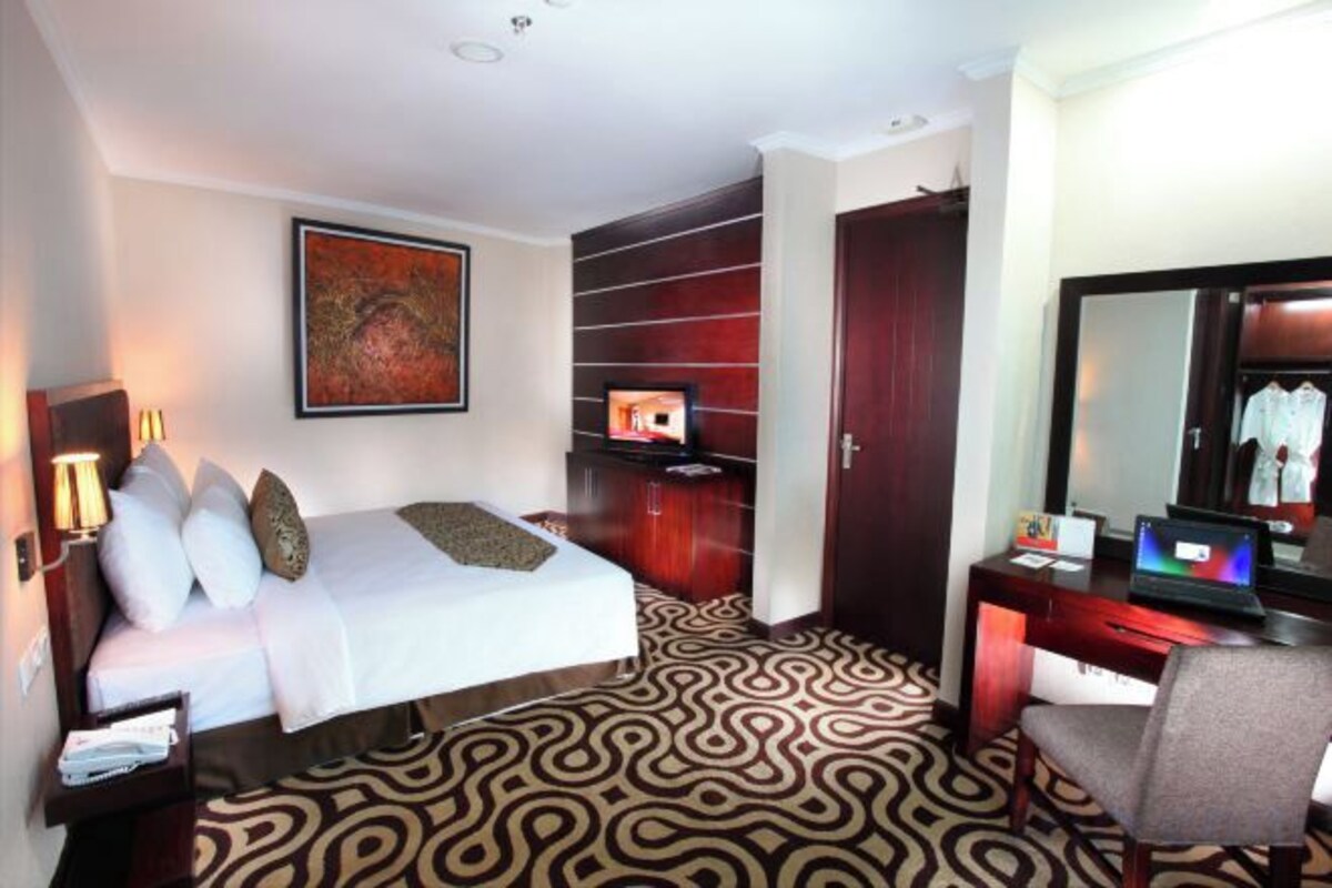 A hotel room with a bed, a desk, a chair, a wardrobe, and a television.