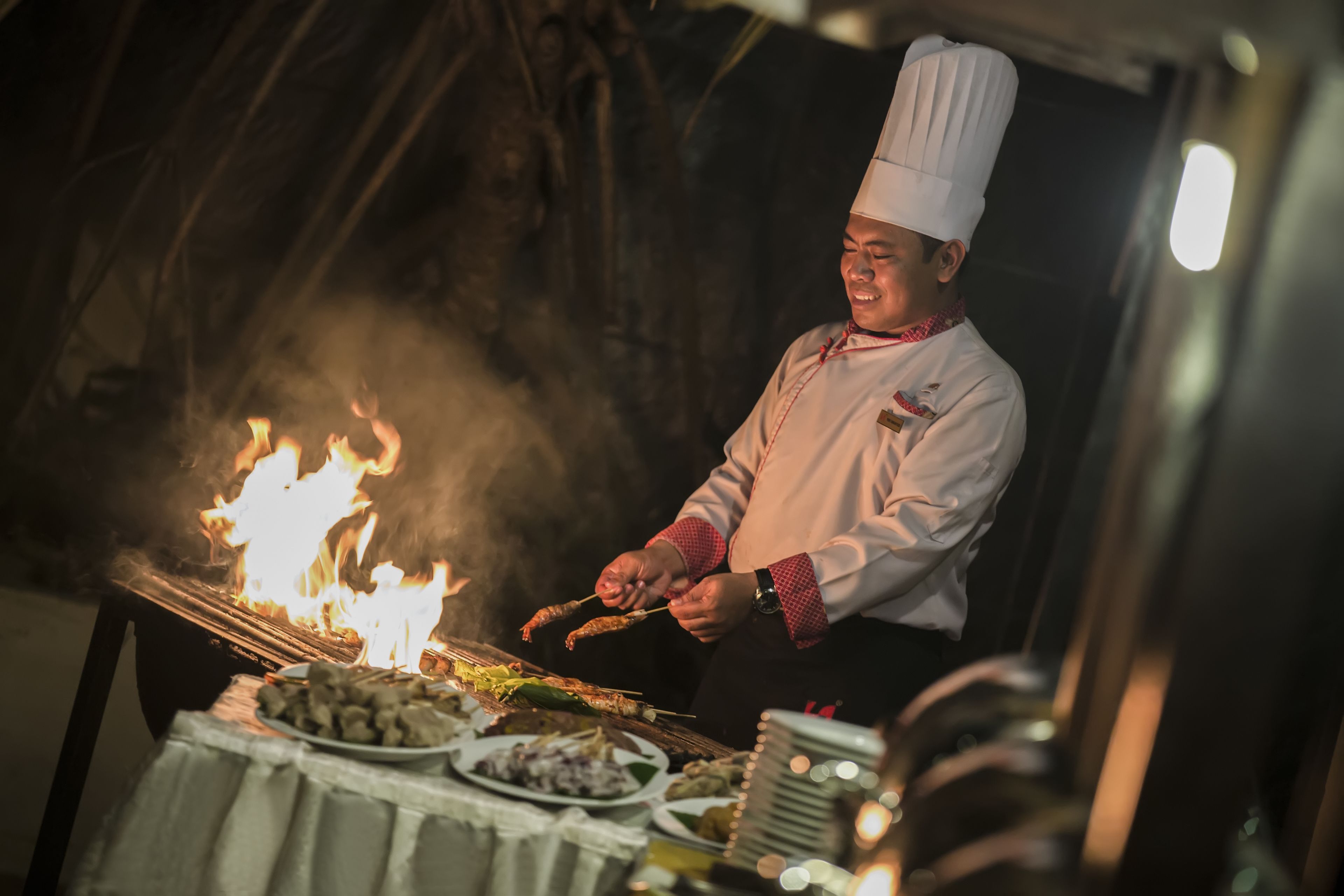 Un chef cuisinant des aliments sur un grill à l’extérieur, au-dessus d’un feu.