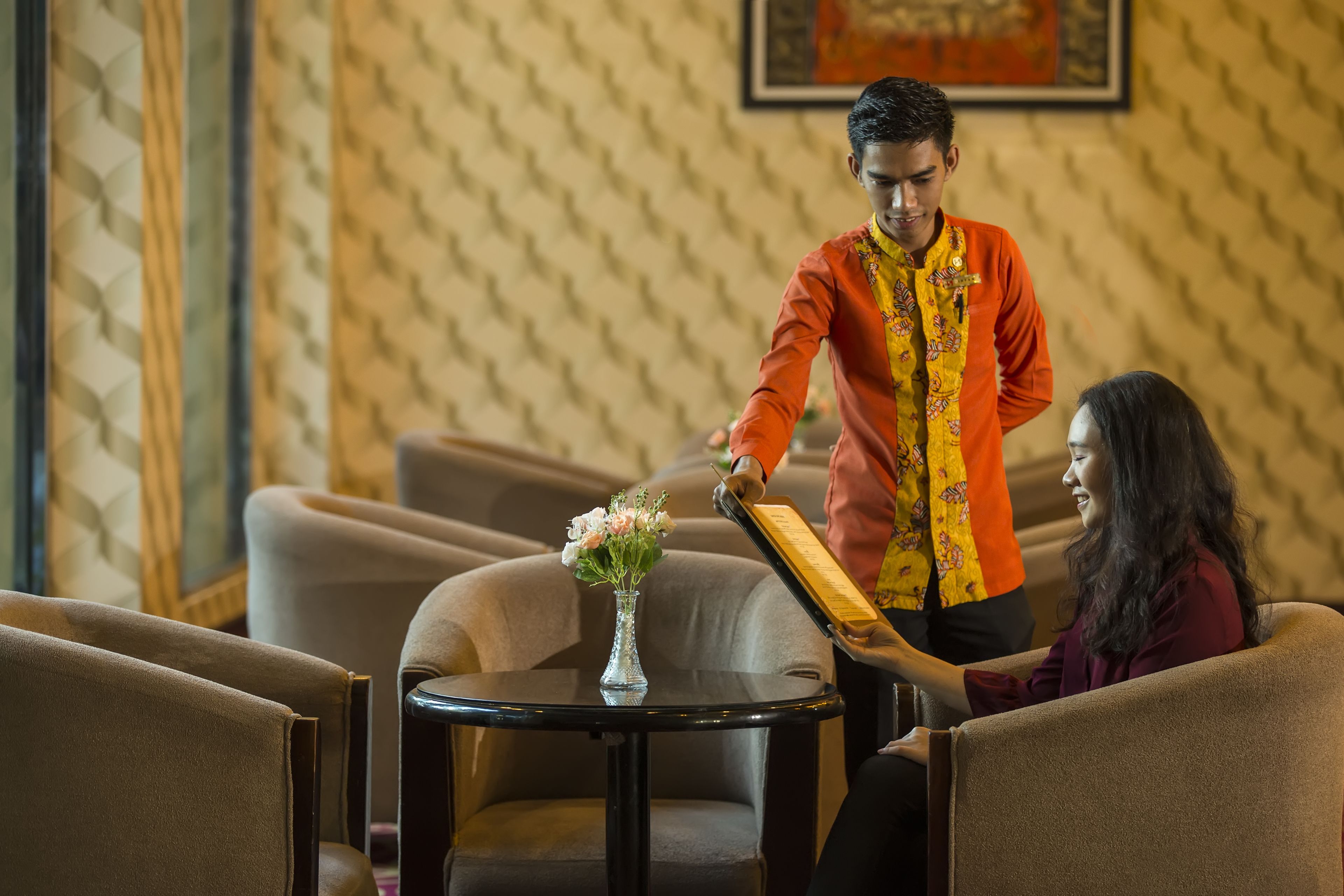 A hotel lobby with a round table, a vase of flowers, and a person standing next to a chair.