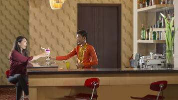 Angolo bar con un barista che serve un drink a un cliente. Sono presenti sgabelli da bar, un bancone e scaffali pieni di bottiglie.