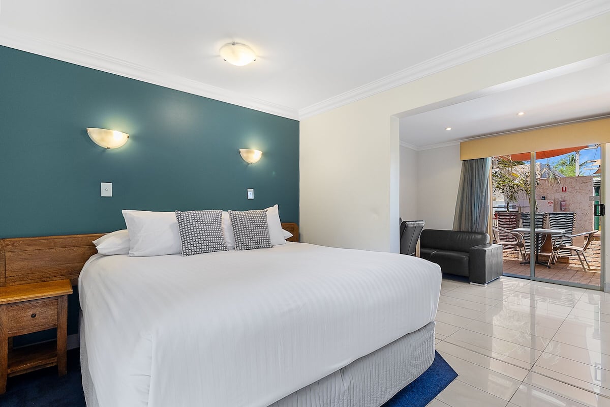 A large bed with white linens, two wall sconces, and a wooden nightstand.