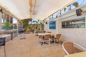 An outdoor patio area with tables and chairs, a bar, and a view of the sea.