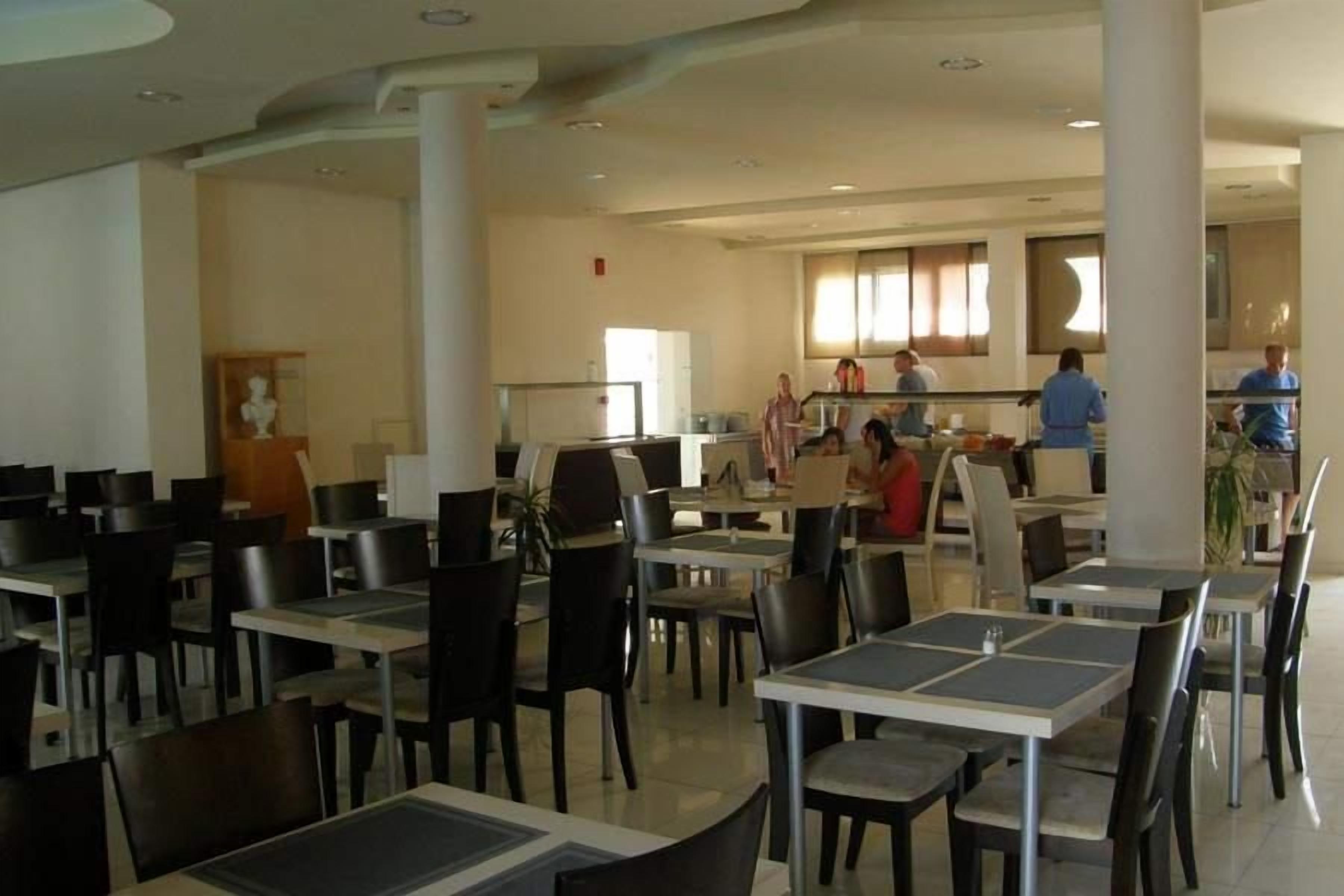 A spacious dining area with multiple tables and chairs, a counter with staff, and a view of the kitchen in the background.