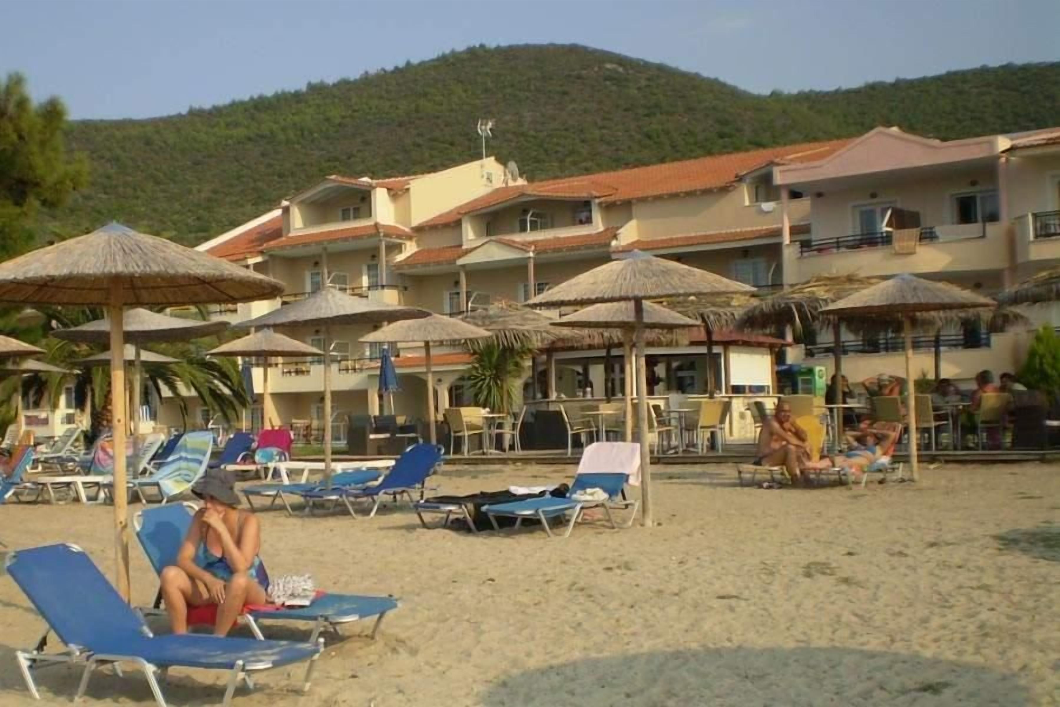A beachside hotel with multiple balconies, sun loungers, and thatched umbrellas.