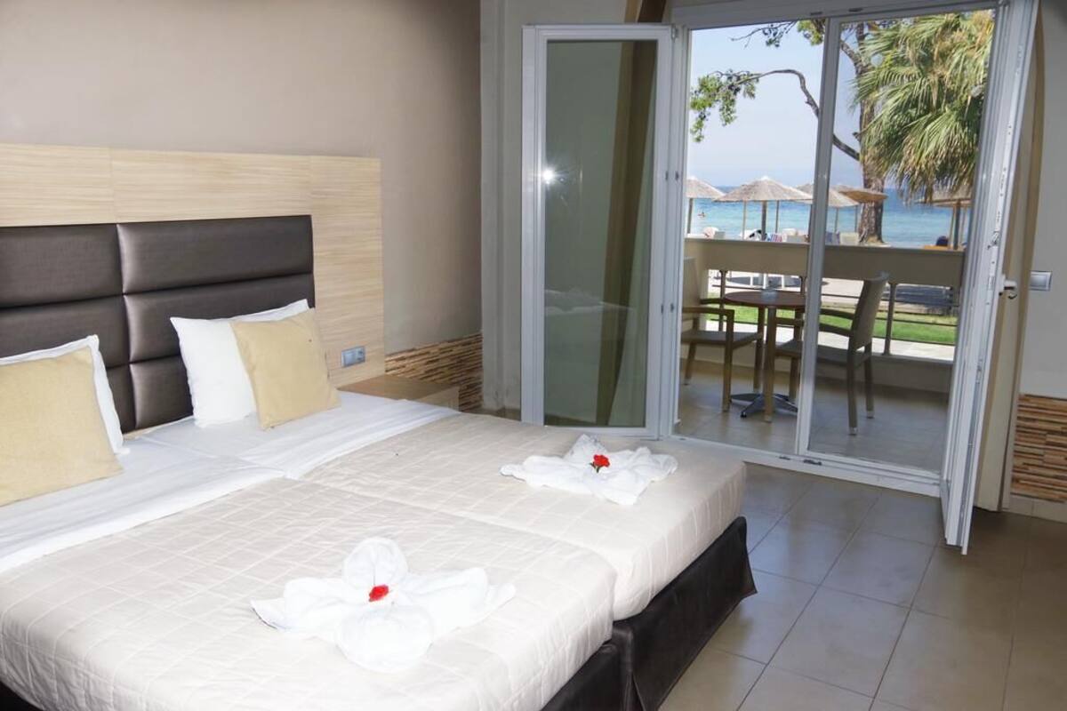 Habitación de hotel con una cama grande, una puerta corrediza al balcón y vista a la playa.