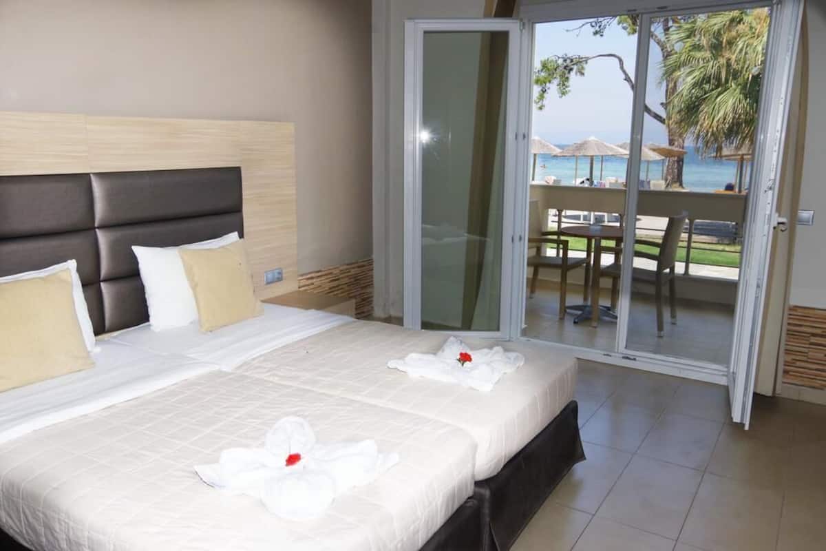 Une chambre d’hôtel avec un grand lit, une porte-fenêtre coulissante donnant sur un balcon et une vue sur la plage.