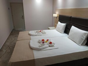Quarto de hotel com duas camas, cada uma com uma toalha dobrada e um pequeno buquê de flores.
