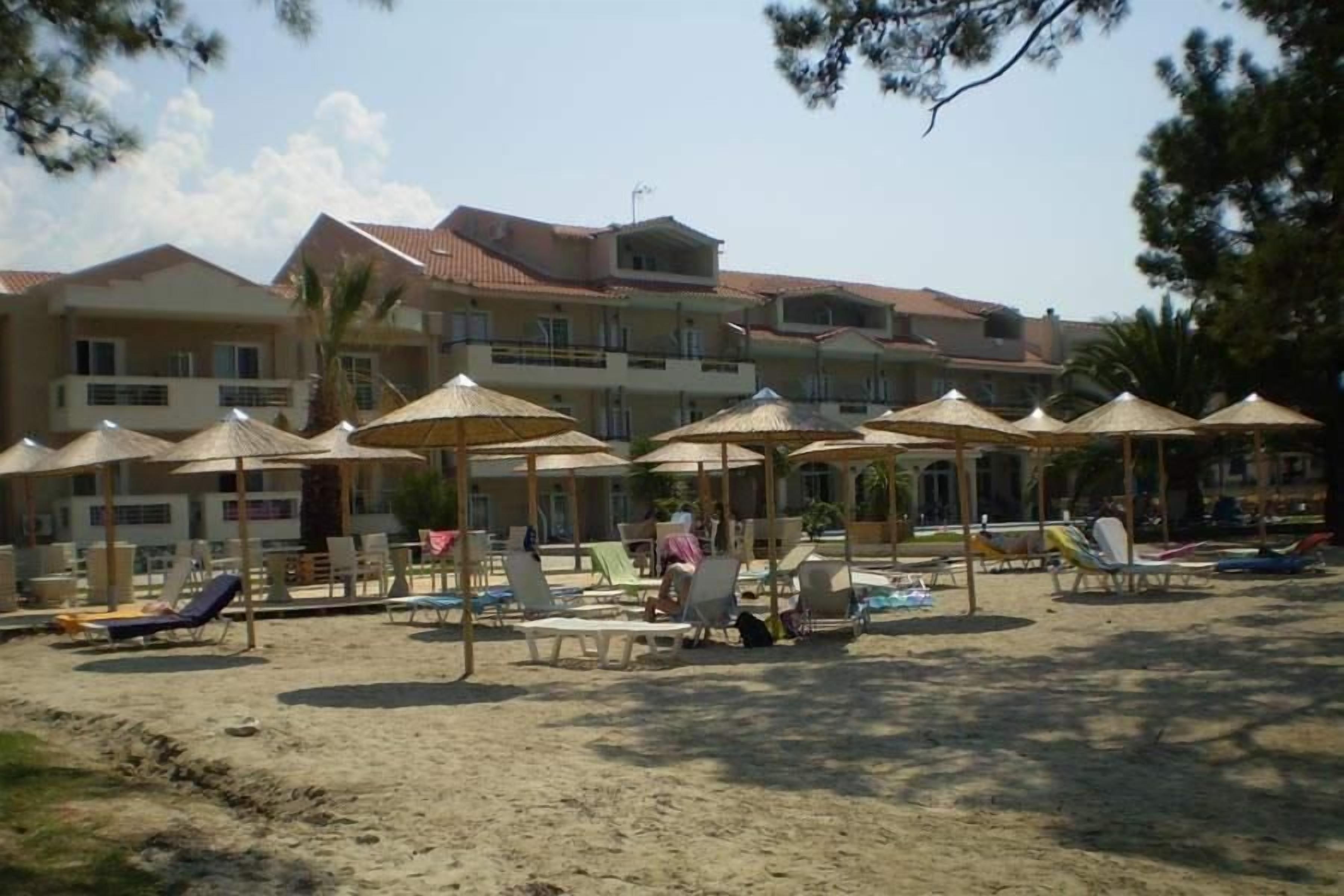 A beachside hotel with multiple lounge chairs and umbrellas, a sandy beach, and a building with a tiled roof.