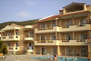 A multi-story hotel with a swimming pool, balconies, and a hilly backdrop. - Rachoni Resort (Thasos)