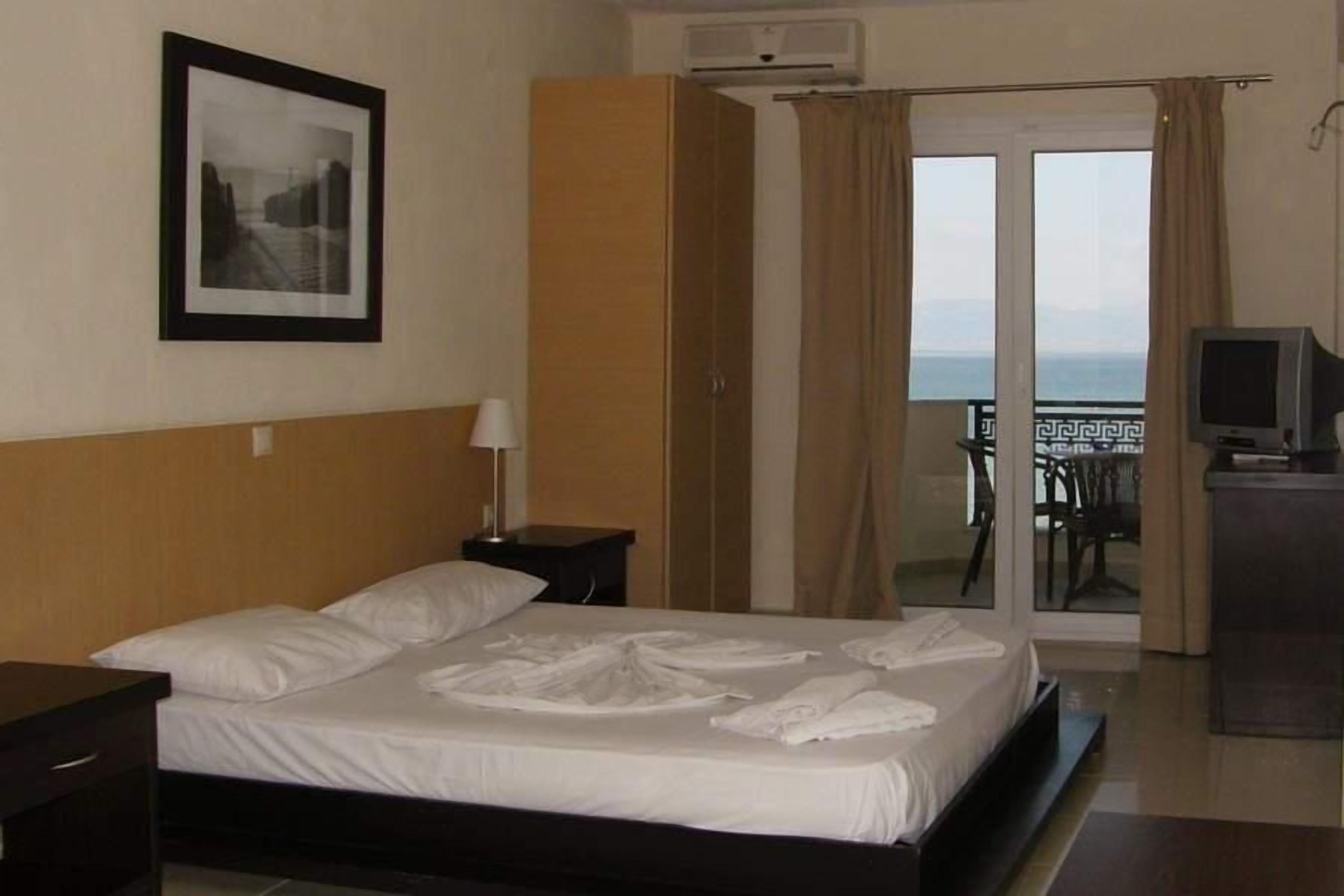 A hotel room with a bed, a television, a picture on the wall, and a view of the sea through the window.