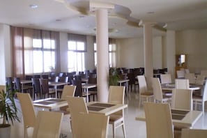 A spacious dining area with multiple tables and chairs, large windows, and a modern ceiling design. - Rachoni Resort (Thasos)