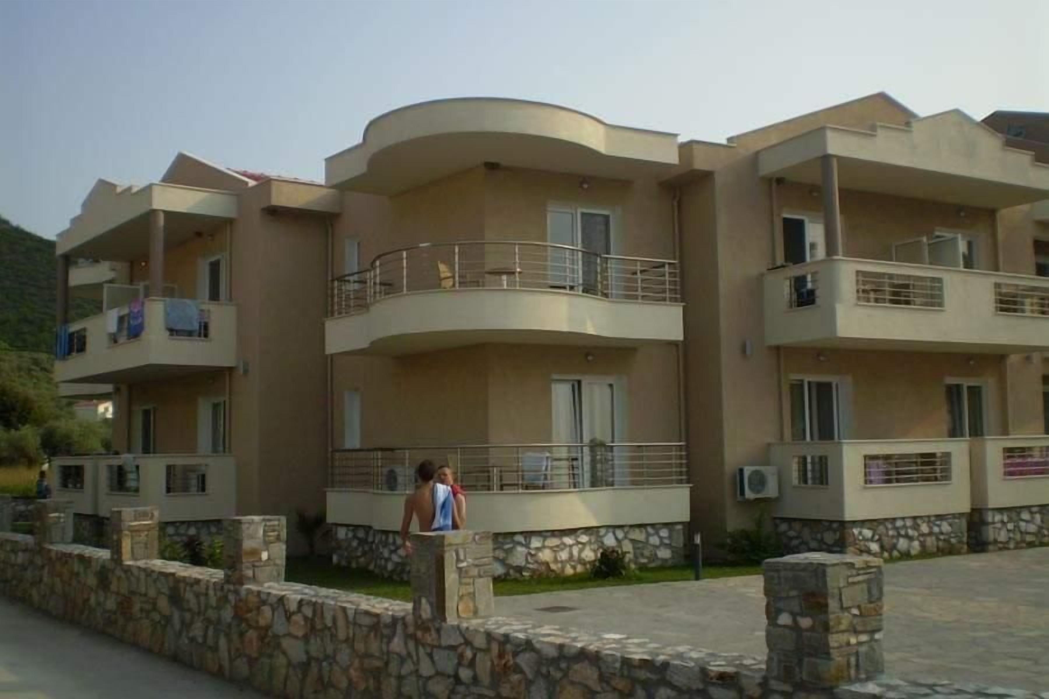 A multi-story residential building with balconies, stone walls, and a clear sky.