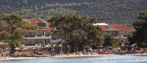 Un hotel frente al mar con varios balcones, asientos en la playa y vistas al océano.