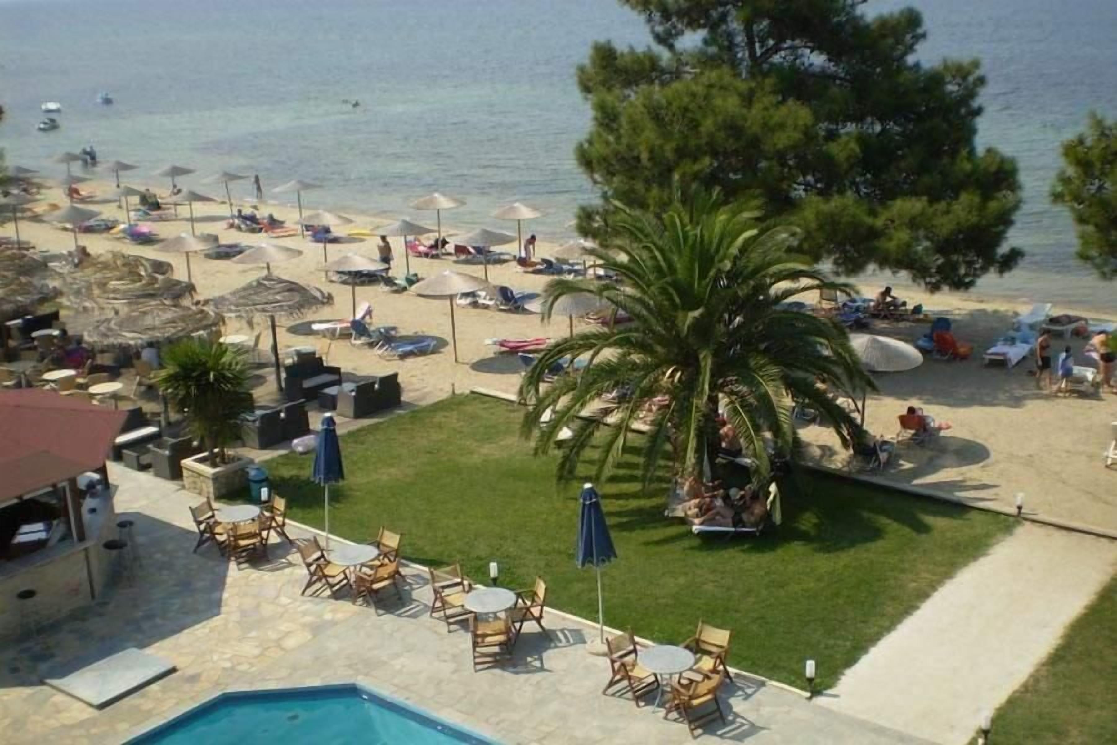 A beachside hotel with a pool, lounge chairs, umbrellas, and a view of the sea.