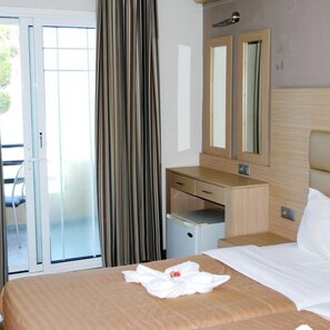 Quarto de hotel com cama, escrivaninha, cadeira, mini-frigorífico, porta de vidro deslizante e espelho.
