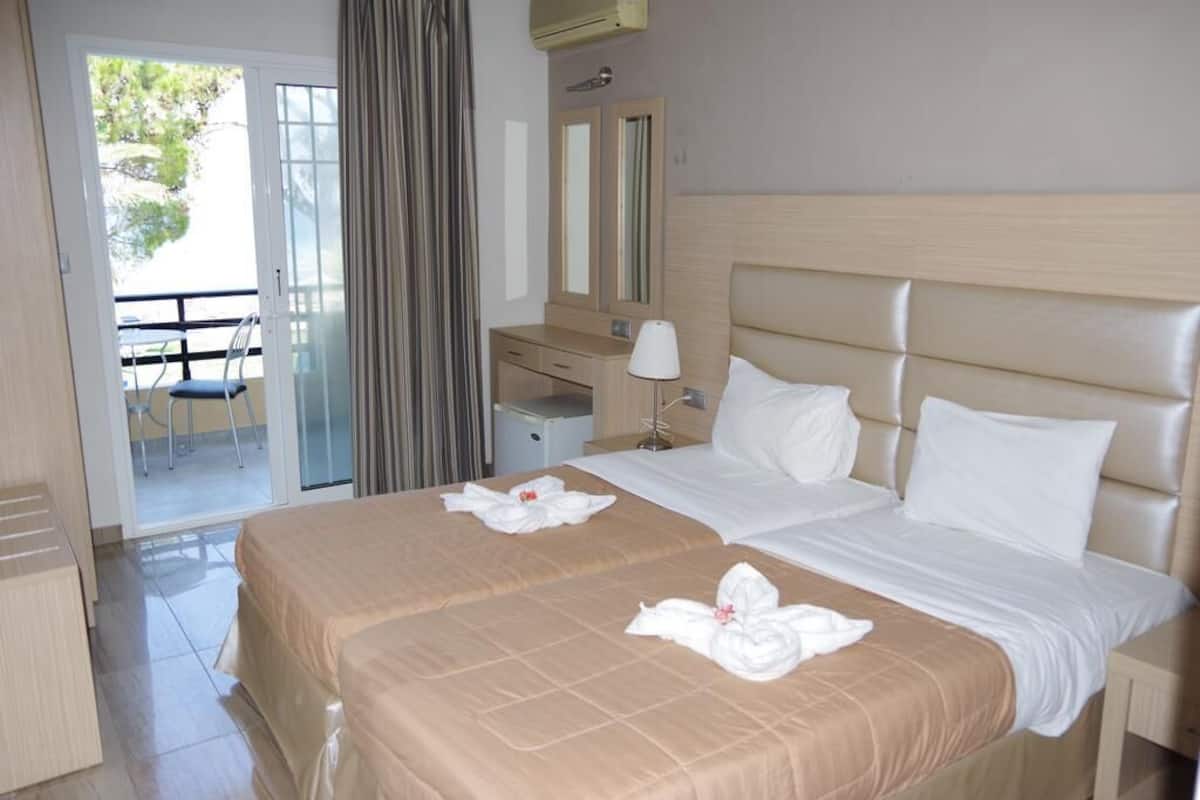 Habitación de hotel con dos camas, un escritorio, una silla y un balcón.