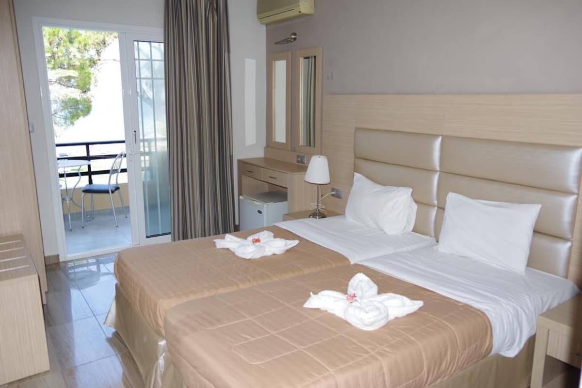 A hotel room with two beds, a desk, a chair, and a balcony.