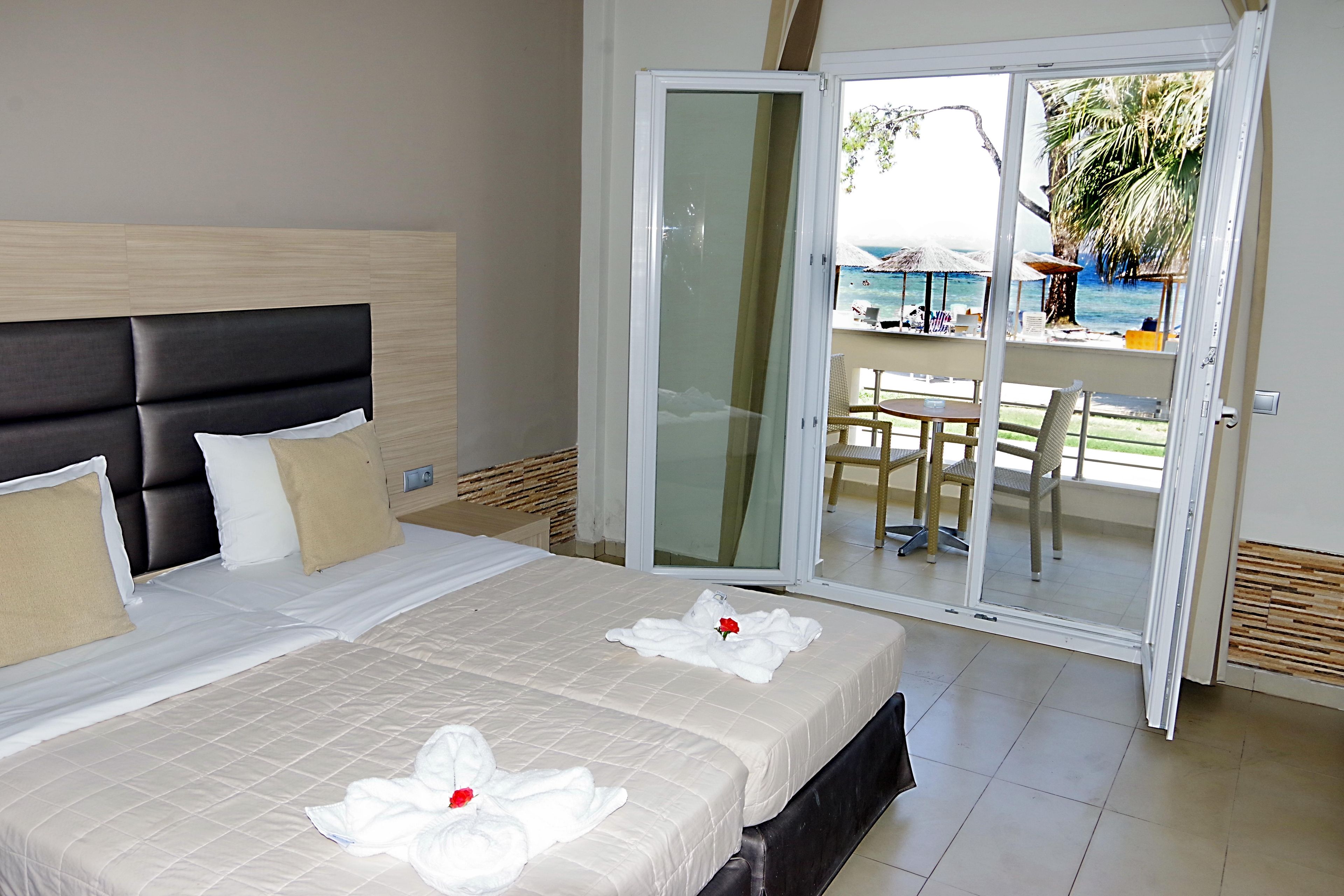 Habitación de hotel con una cama, puerta corrediza de vidrio que da a un balcón con vistas a la playa y sombrillas.