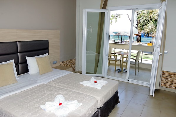 Quarto de hotel com cama, porta de vidro deslizante que dá para uma varanda com vista para a praia e guarda-sóis.