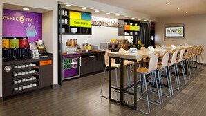 Een moderne hotel lobby met een koffieautomaat, een receptiebalie en een lange tafel met stoelen voor dineren.