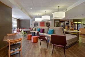 Ein modernes Interieur mit einer Sitzecke, die eine Couch und Sessel umfasst, einem Essbereich mit Tischen und Stühlen sowie einer Theke mit einer Präsentation.