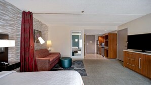 Een hotelkamer met een bed, een bank, een bureau met lamp, een televisie en een kitchenette.