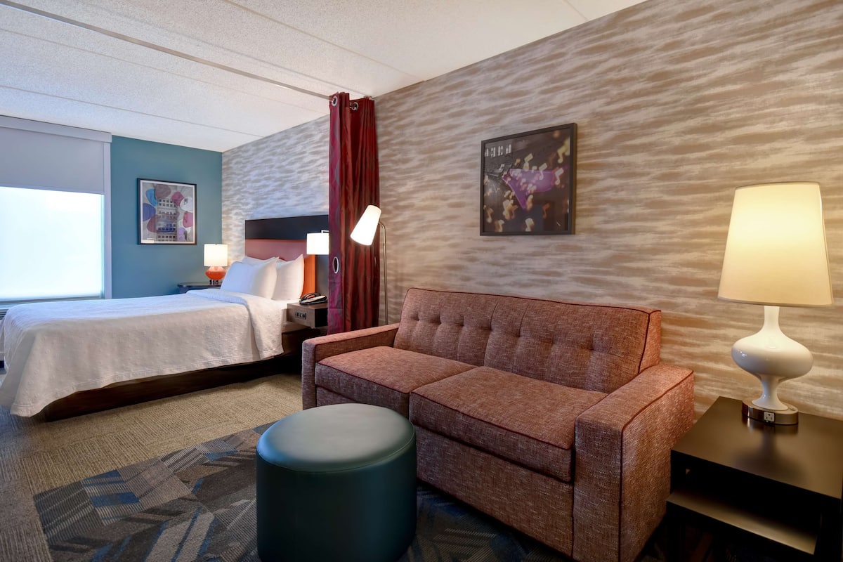 Habitación de hotel con cama, sofá, mesita de noche, lámpara y pared con textura.