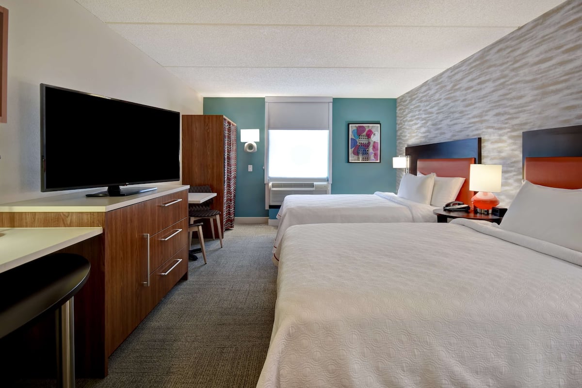 Una habitación de hotel con televisión, escritorio, dos camas y ventana.