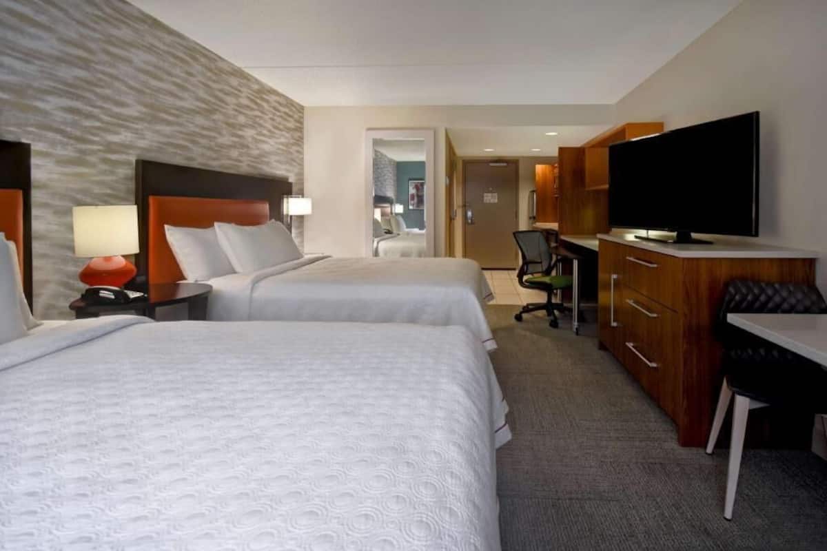 Habitación de hotel con dos camas, un escritorio, televisor y baño visible a través de una puerta abierta.