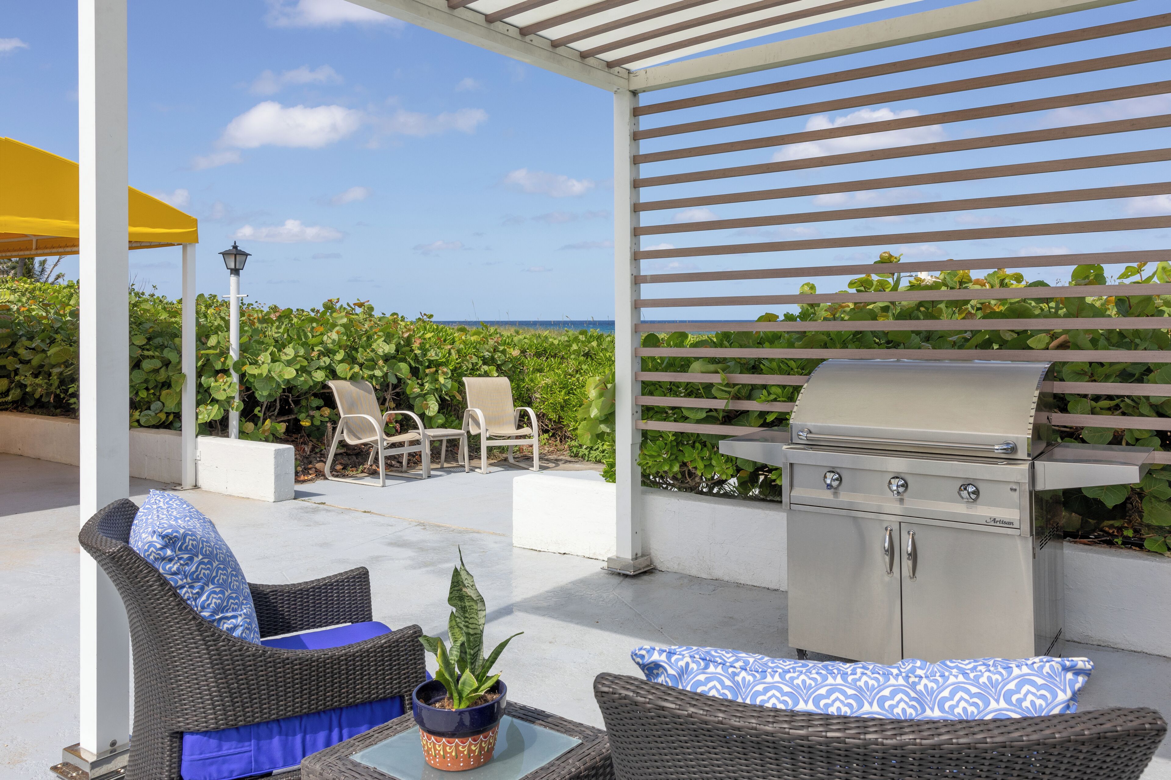 An outdoor patio with a grill, wicker furniture, and a view of the ocean.