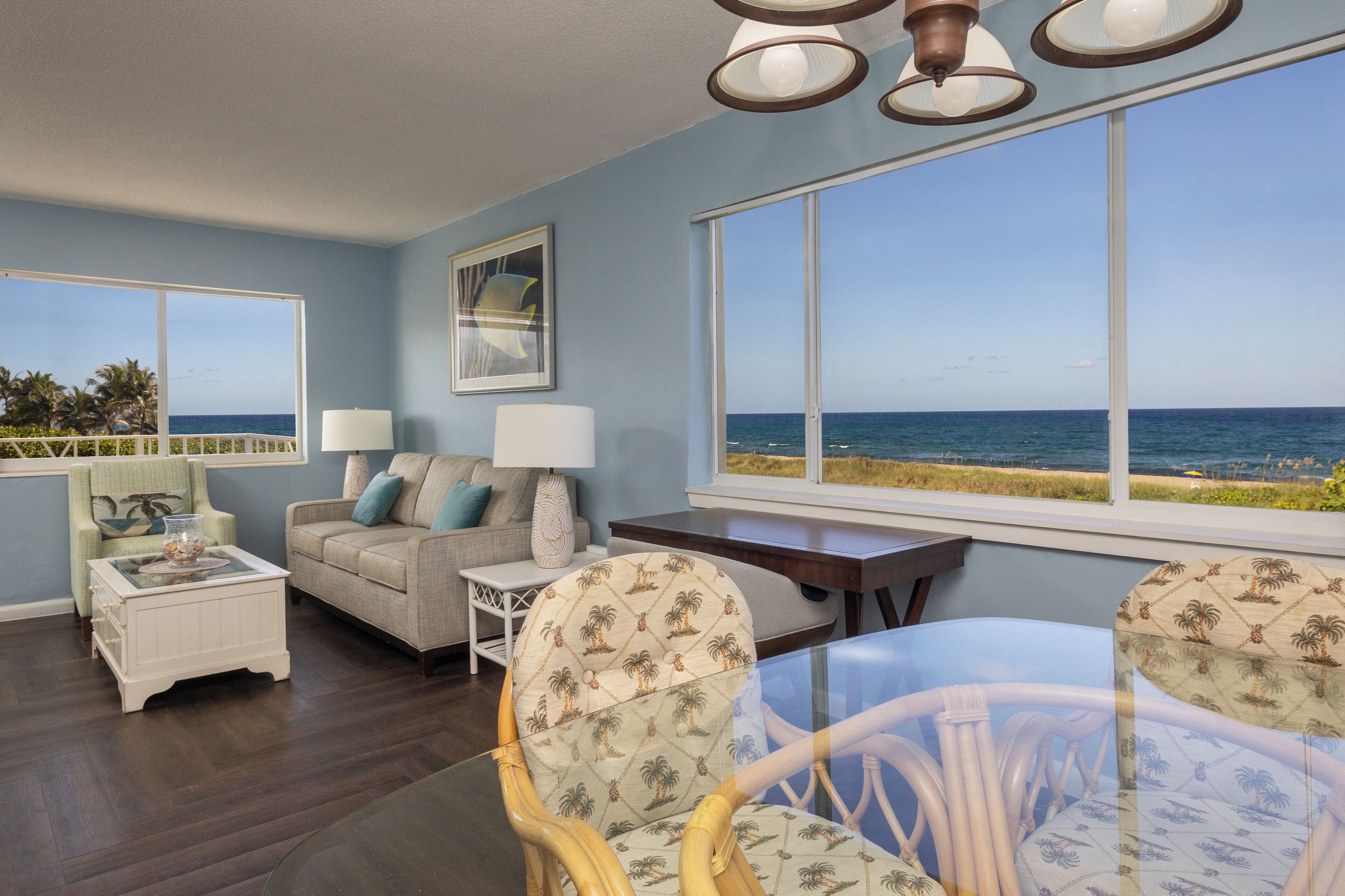 A living room with a view of the ocean, a sofa, a coffee table, and a dining table with chairs.