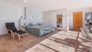 Un dormitorio con una cama, dos sillas, una mesita y un baño visible a través de una puerta abierta.