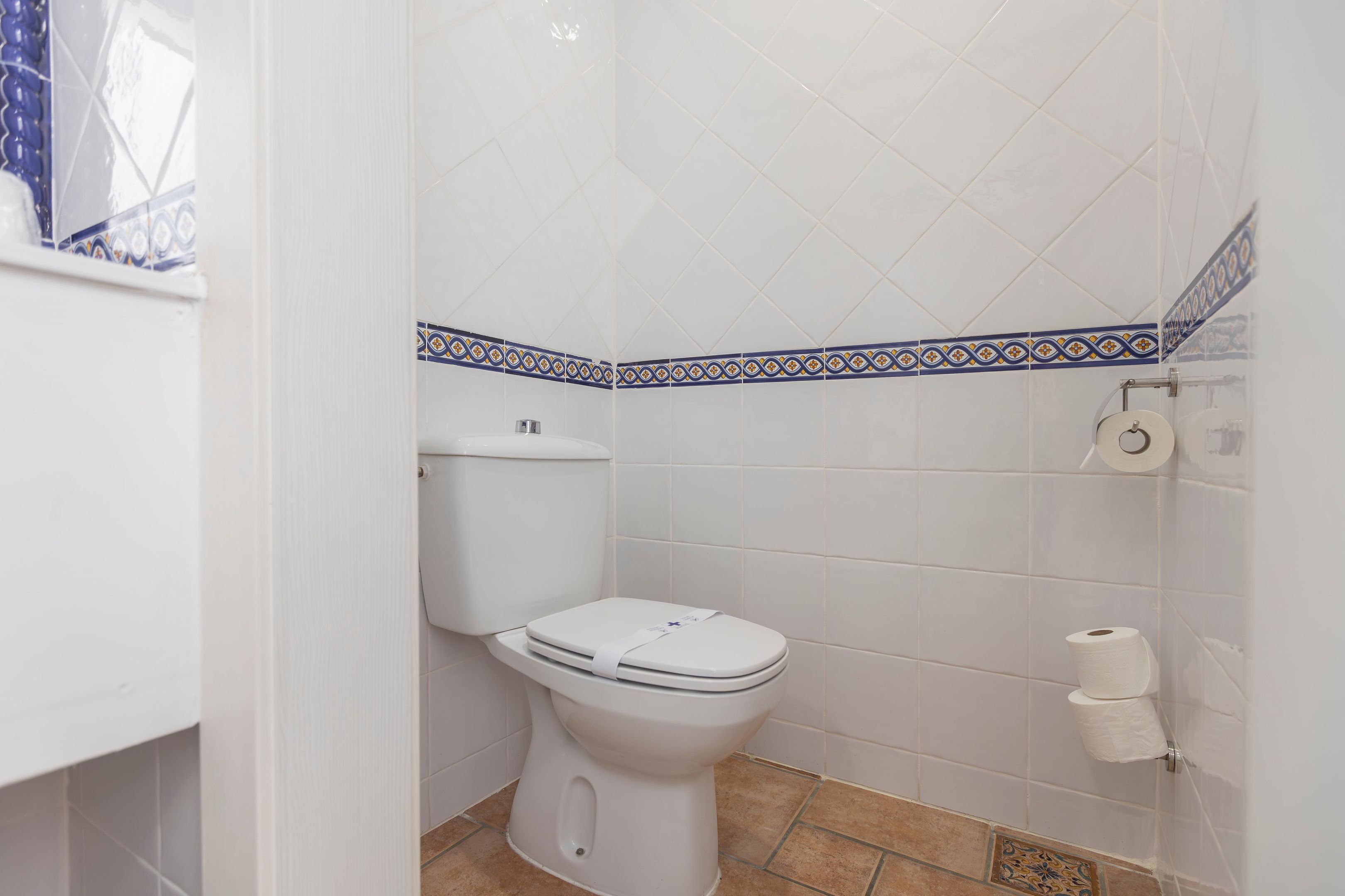 Ein Badezimmer mit Toilette, einer Toilettenrolle und einem gemusterten Fliesenrand.