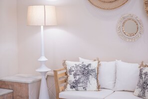 Une pièce avec un lampadaire blanc, une chaise en bois et un canapé blanc agrémenté de coussins à motifs.
