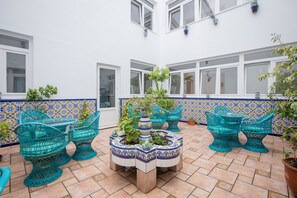 Un patio con mesas al aire libre, plantas en macetas y suelo de baldosas.