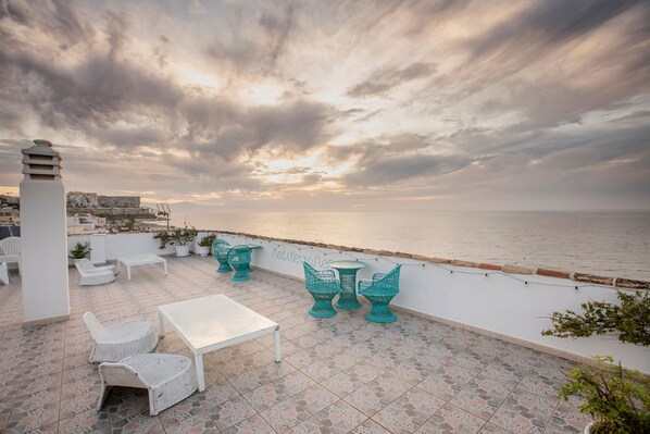 Una terraza con asientos al aire libre, vista al mar y un paisaje urbano de fondo.