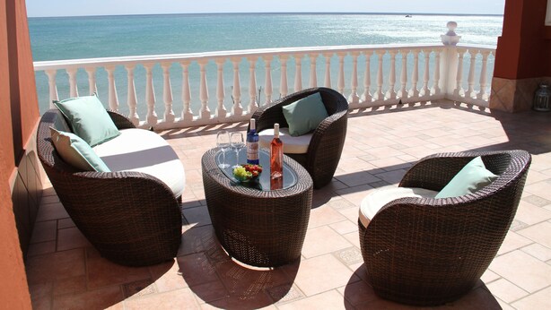 Un balcón con mobiliario de mimbre, una mesa de vidrio y vistas al mar.