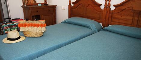 Un dormitorio con dos camas, un aparador y una cesta de mimbre con un sombrero en el lado izquierdo.